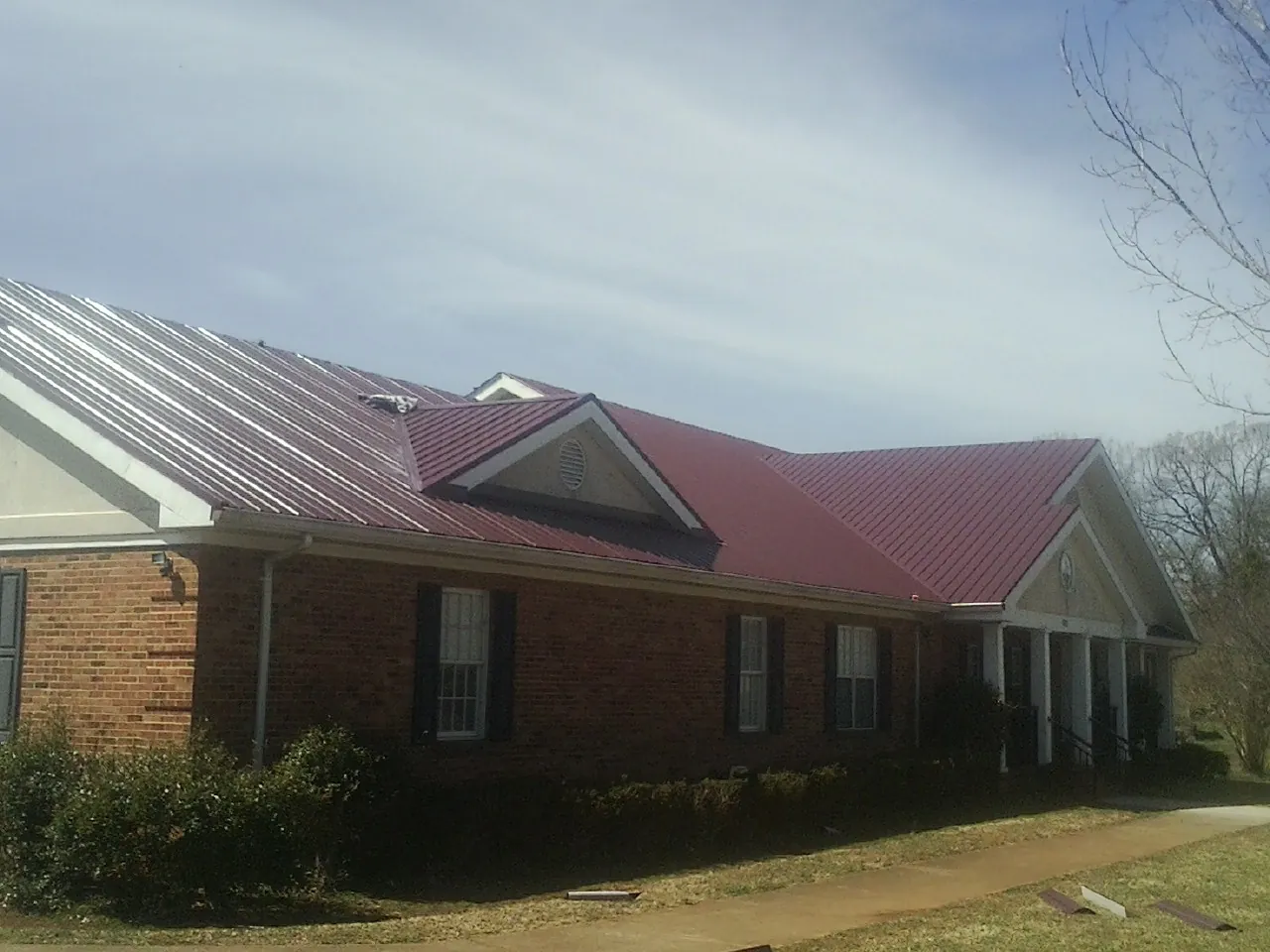 Red metal roof with gabled entries on a long brick building, from a Hail Damage Roof Repair job in Vinegar Bend