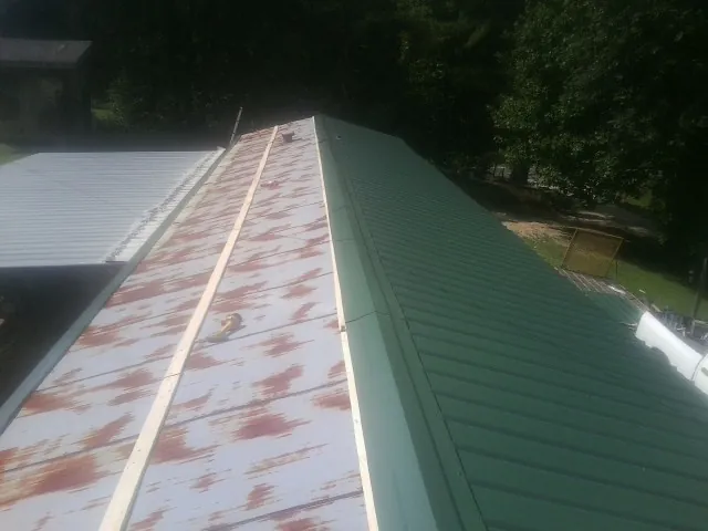 Old rusted panels beside newly installed green metal roofing — Wind Damage Roof Repair by Roofing Brothers in Vinegar Bend