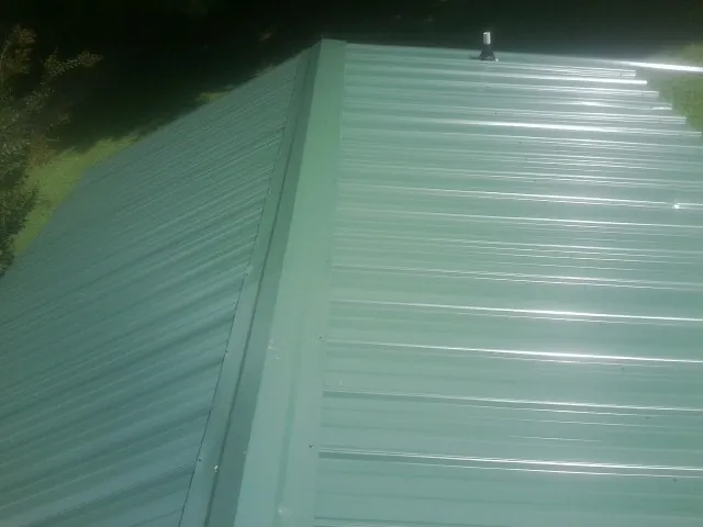 New green metal panels meeting at the ridge of a roof — Flat Roof Repair work by our crew in Vinegar Bend