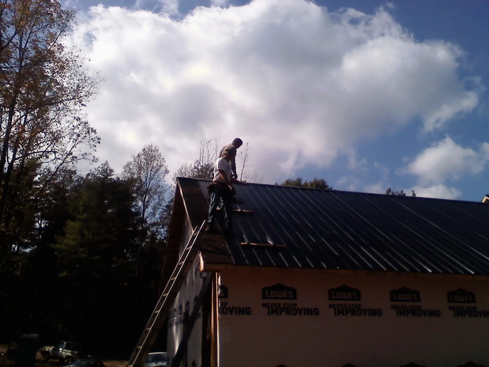 Roofer fastening dark metal panels high against a cloudy sky, from a Roof Inspection job in Vinegar Bend