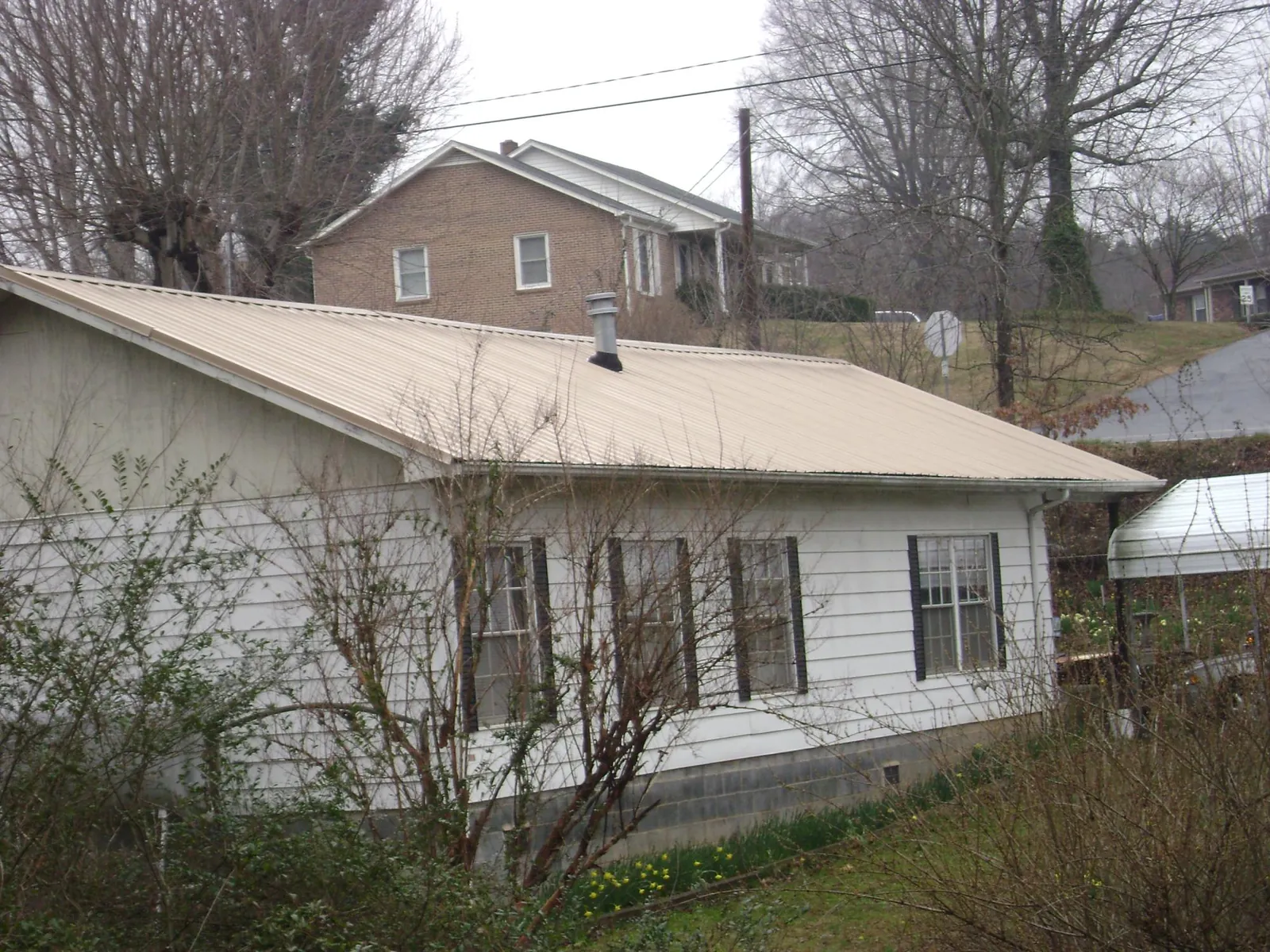 Tan metal roof on a white sided house set into a hillside — Commercial Roofing by Roofing Brothers in Vinegar Bend