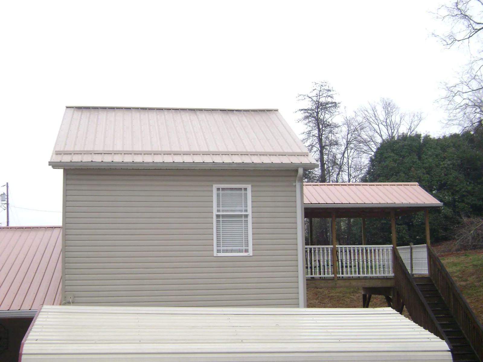 Tan metal roofs on a two story addition and attached porch, from a Roof Replacement job in Vinegar Bend